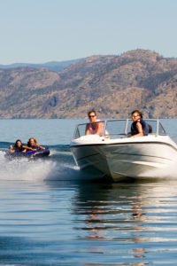 Boat on a lake pulling two people on an inflatable tube.