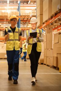 A man and woman in hard hats walking through a warehouse