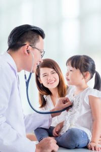 Doctor listening to young girl's breathing with mother next to her.