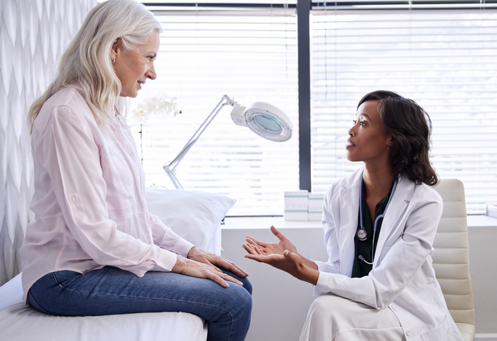 Mature Woman In Consultation With Female Doctor Sitting On Examination Couch In Office Woman In Consultation With Female Doctor